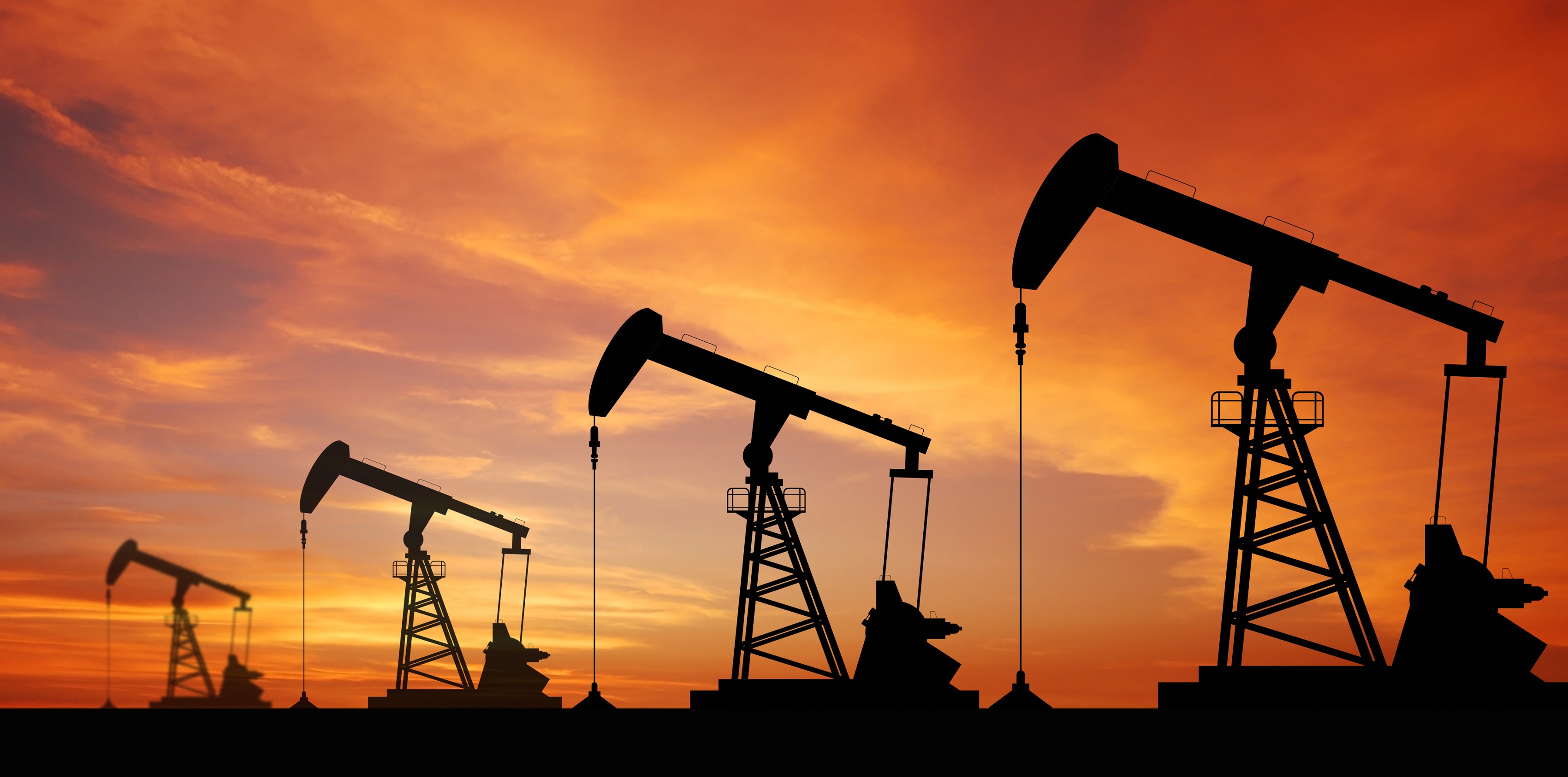 Oil pump jacks silhouetted against an orange sunset